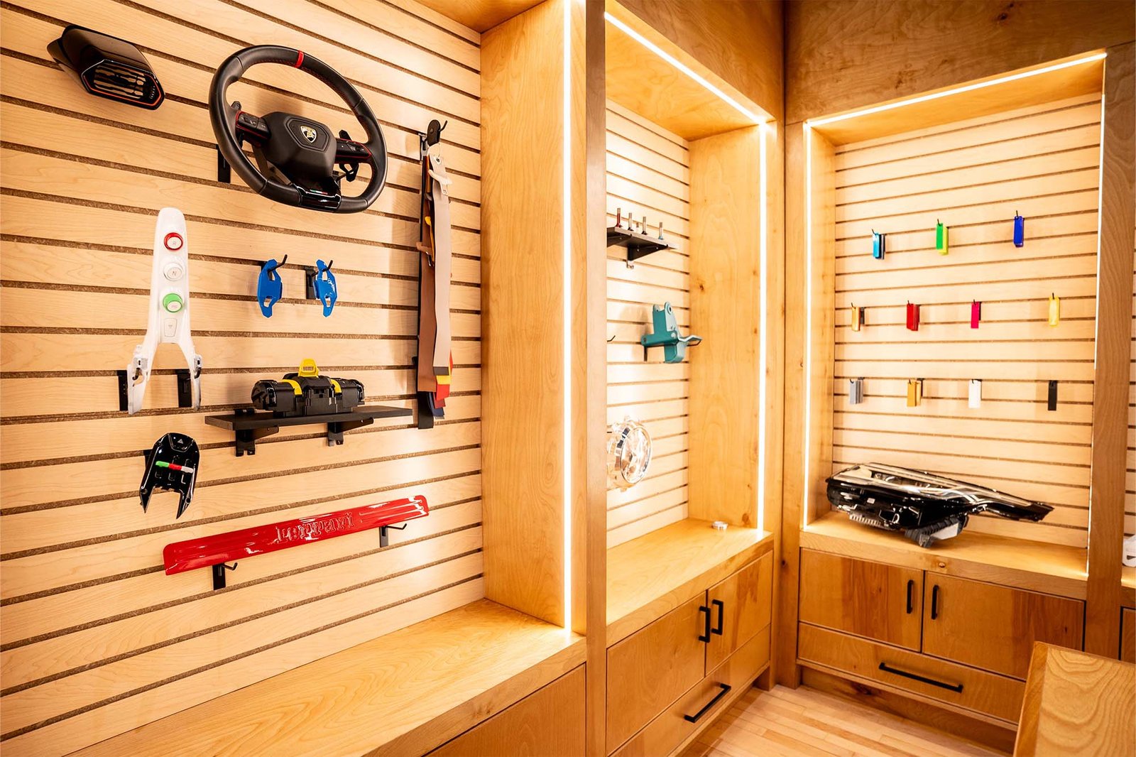 Display of automotive tools and accessories on wooden slat walls, featuring a steering wheel, various car parts, and colorful tool organizers, showcasing the meticulous design and craftsmanship of Aesthetics Auto Solutions' facility.