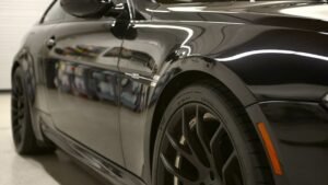 Black luxury car showcasing a glossy finish, highlighting the ceramic coating's protective qualities and aesthetic appeal, with sleek black rims and a polished surface reflecting surrounding light.