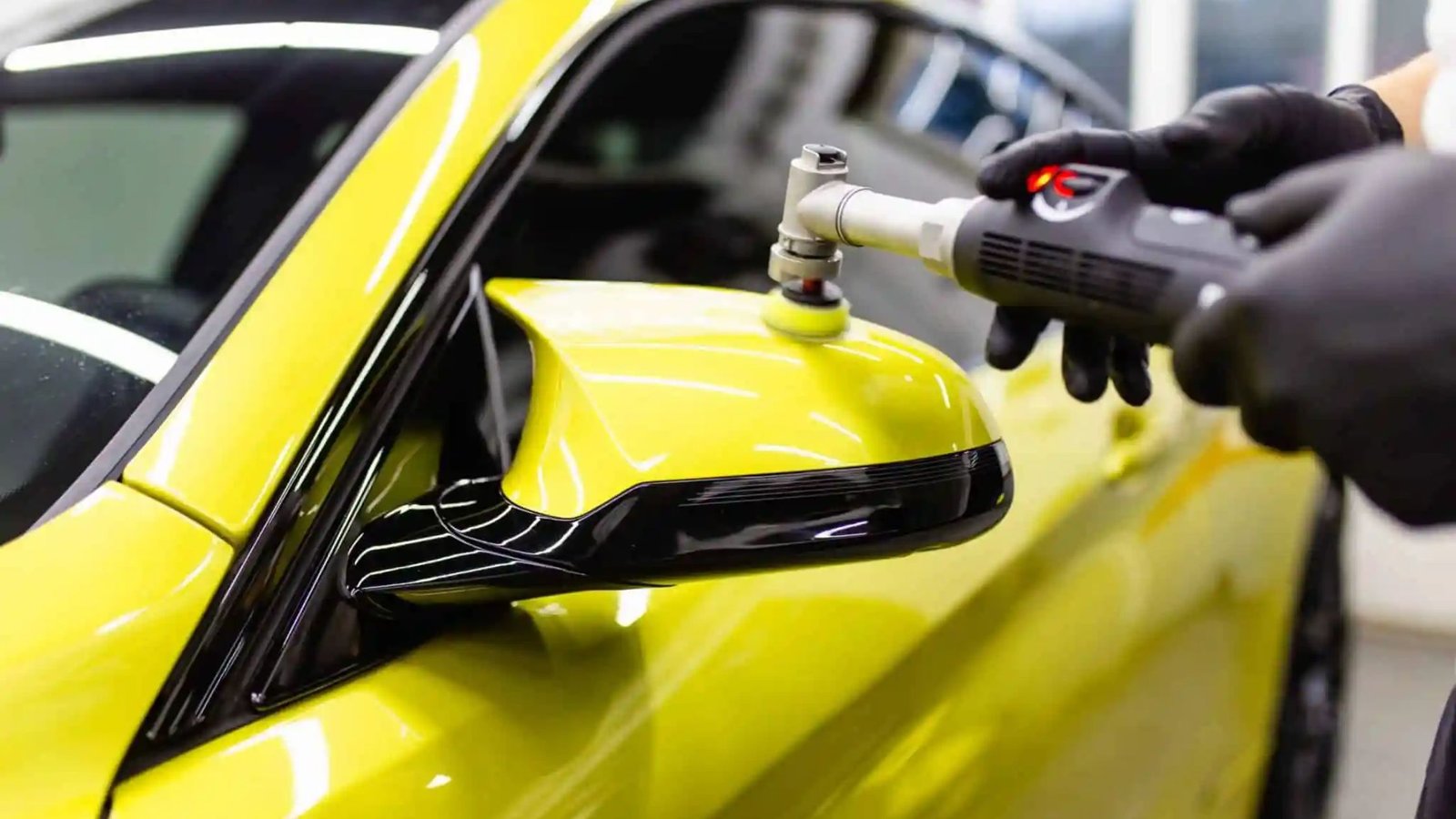 Person using a polishing tool on a yellow car mirror, demonstrating paint correction techniques for automotive detailing services.