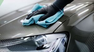 Person in black gloves polishing a car hood with a blue microfiber cloth, emphasizing professional car detailing services.