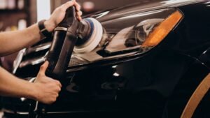 Hands using a polishing machine on the headlight of a black car, demonstrating professional auto detailing services in West Boylston.