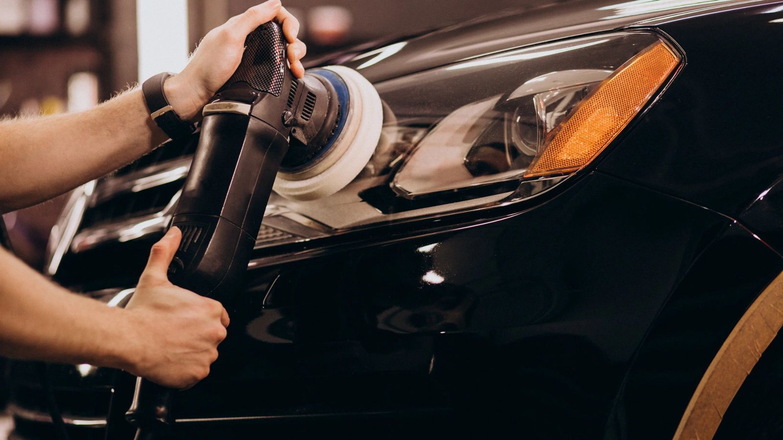 Person using a polishing machine on a black vehicle's headlight, demonstrating professional auto detailing services in West Boylston, MA.