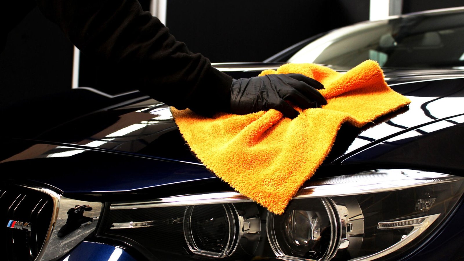Person using an orange microfiber towel to detail a shiny blue car hood, emphasizing vehicle maintenance and auto detailing services in West Boylston, Massachusetts.
