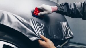 Person applying vinyl wrap to a vehicle's fender using a squeegee, showcasing professional vehicle wrapping techniques in a garage setting.