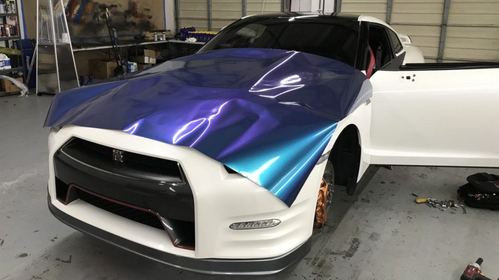 Vinyl wrap being applied to a white sports car, showcasing a vibrant blue and purple design in a vehicle customization workshop.