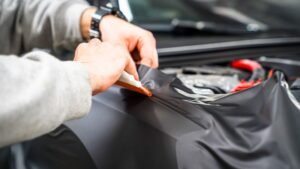 Person applying vinyl wrap to a vehicle hood, showcasing professional vehicle wrapping services by Aesthetic Auto Solutions in West Boylston.