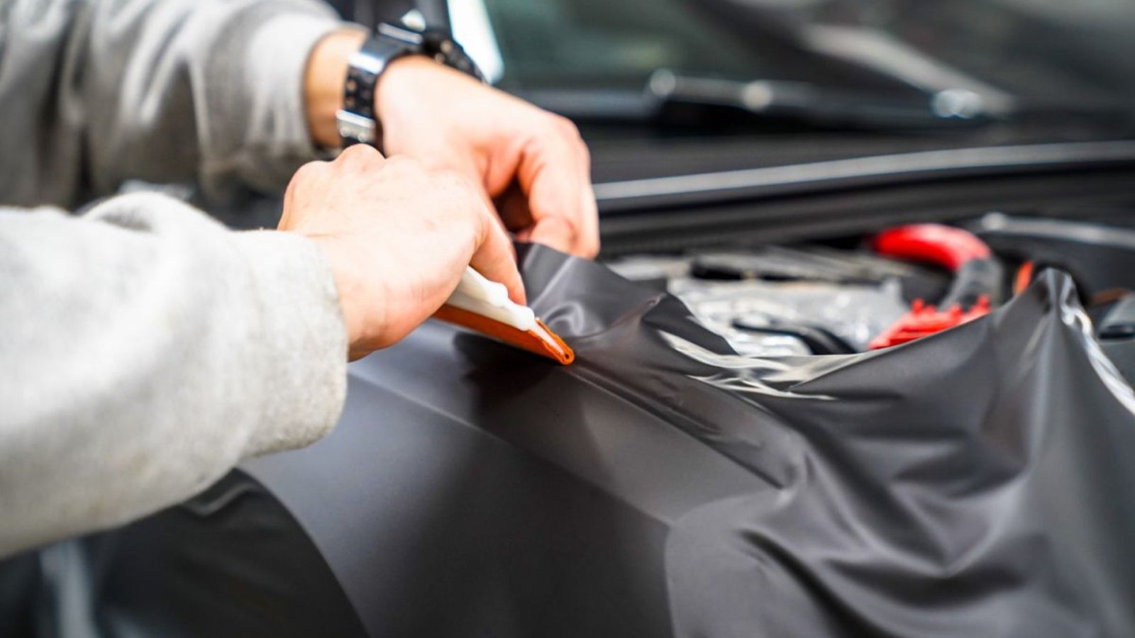 Person applying black vinyl wrap to a vehicle's surface, demonstrating expert vehicle transformation techniques relevant to vinyl wrapping services.